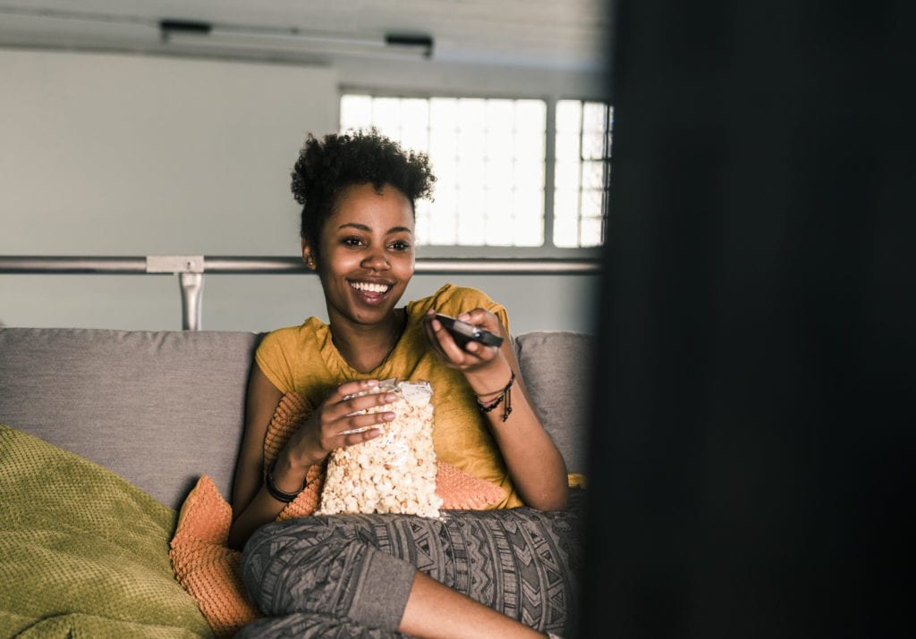 Laughing young woman sitting on couch watching Spectrum TV