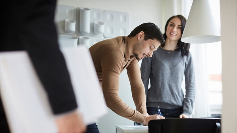 Woman looking at real estate agent while man signing documents at new home