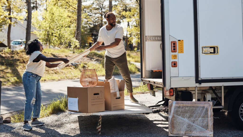 Full length of boyfriend passing picture frame to girlfriend while unloading from van