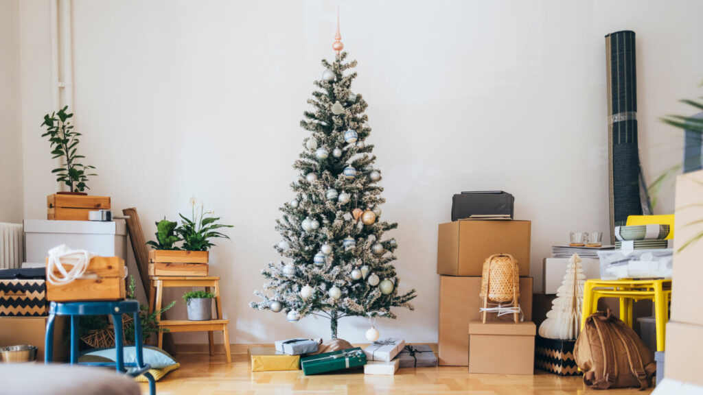 Messy living room full with cardboard boxes and furniture with decorated Christmas tree and presents